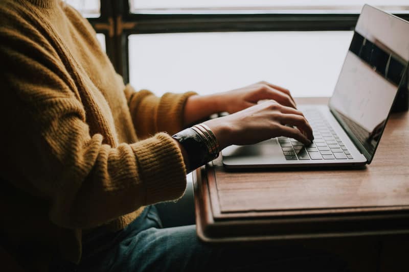 A person typing on a laptop near a window